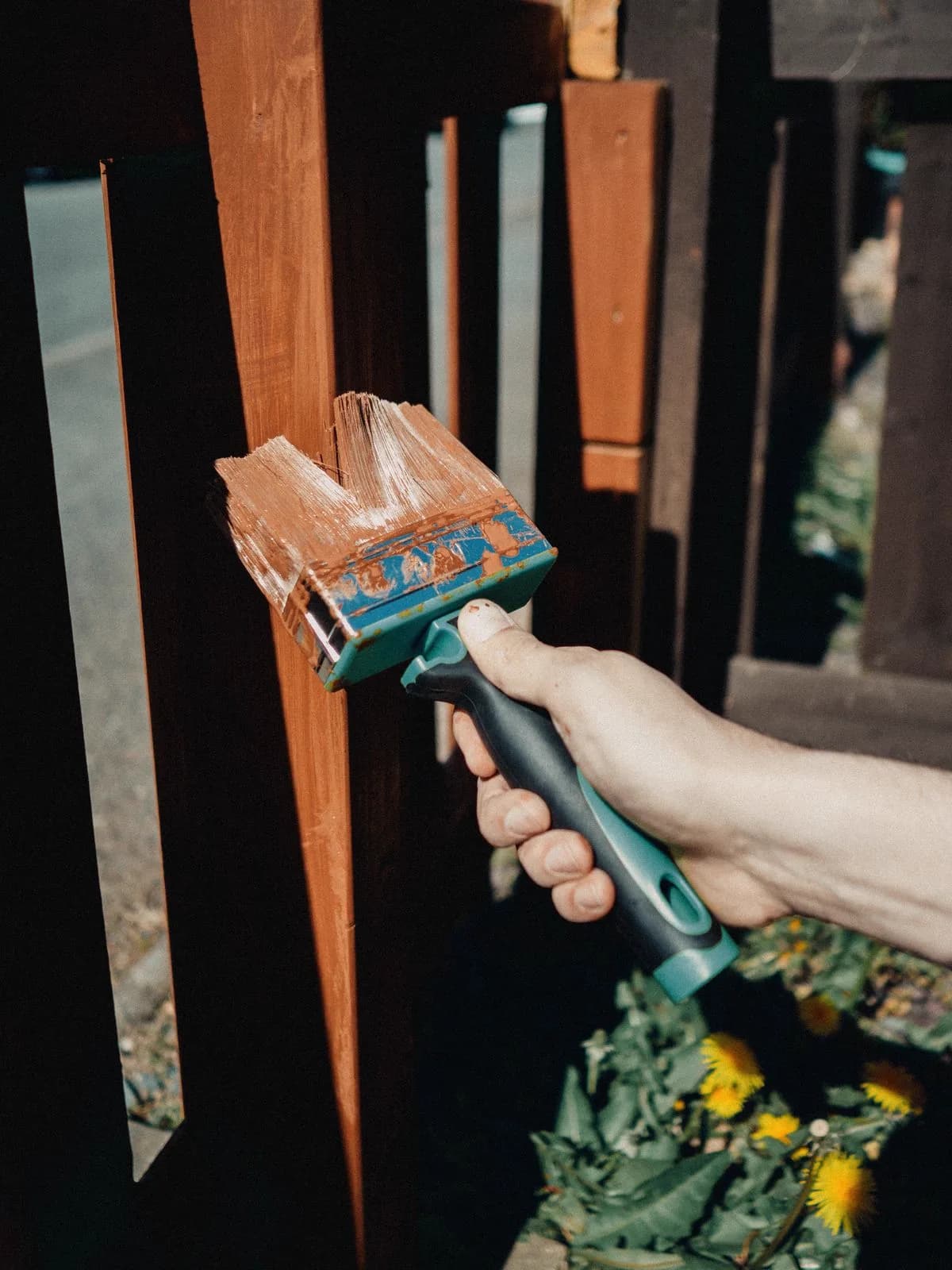 Hand applying stain to a wooden fence with a brush